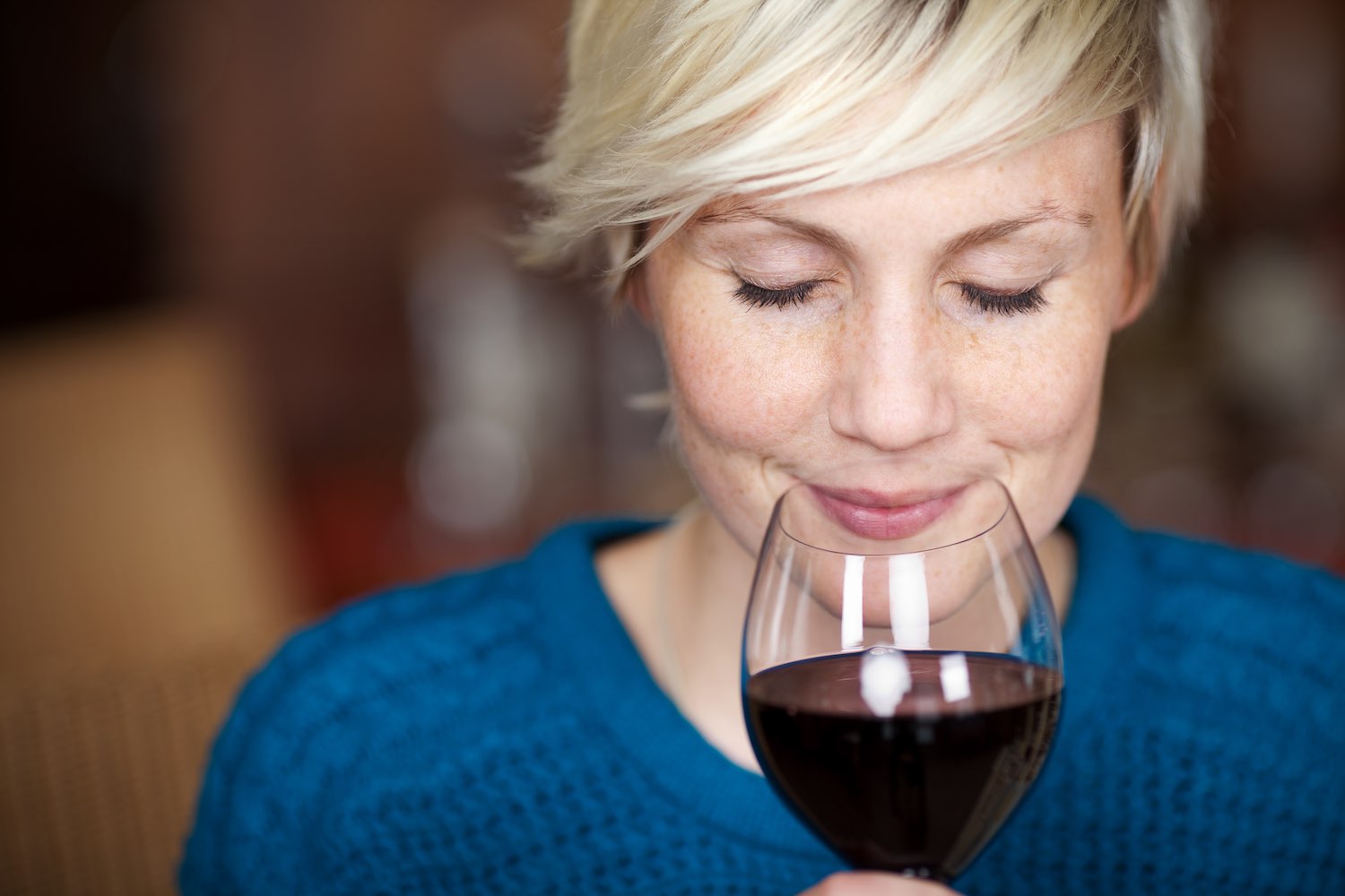 Signora bionda con maglione blu degusta un bicchiere di vino rosso toscano