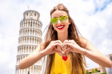Ragazza con le mani a cuore davanti alla Torre di Pisa durante un'estate in Toscana