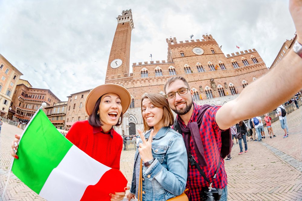 Tre ragazzi in viaggio a Siena in Piazza del Campo con bandiera italiana