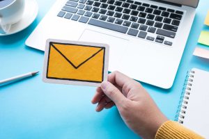 Il concetto di email marketing: mano che tiene busta da lettere gialla con pc sullo sfondo