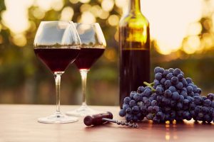 Bicchieri e bottiglia di vino rosso al tramonto con grappolo d'uva