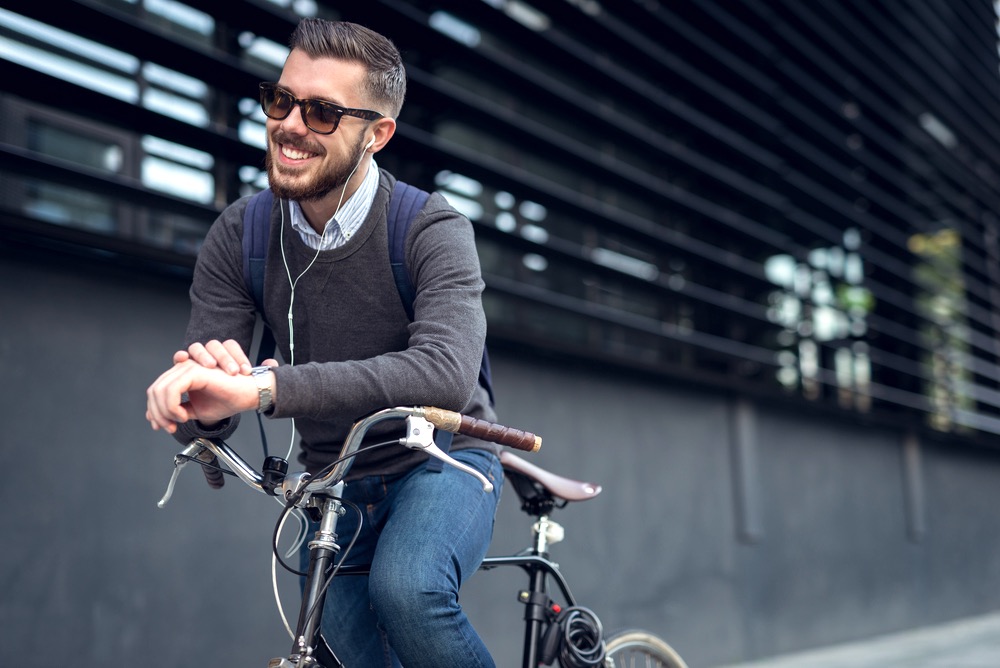 Ragazzo sorride appoggiato a una bicicletta in città