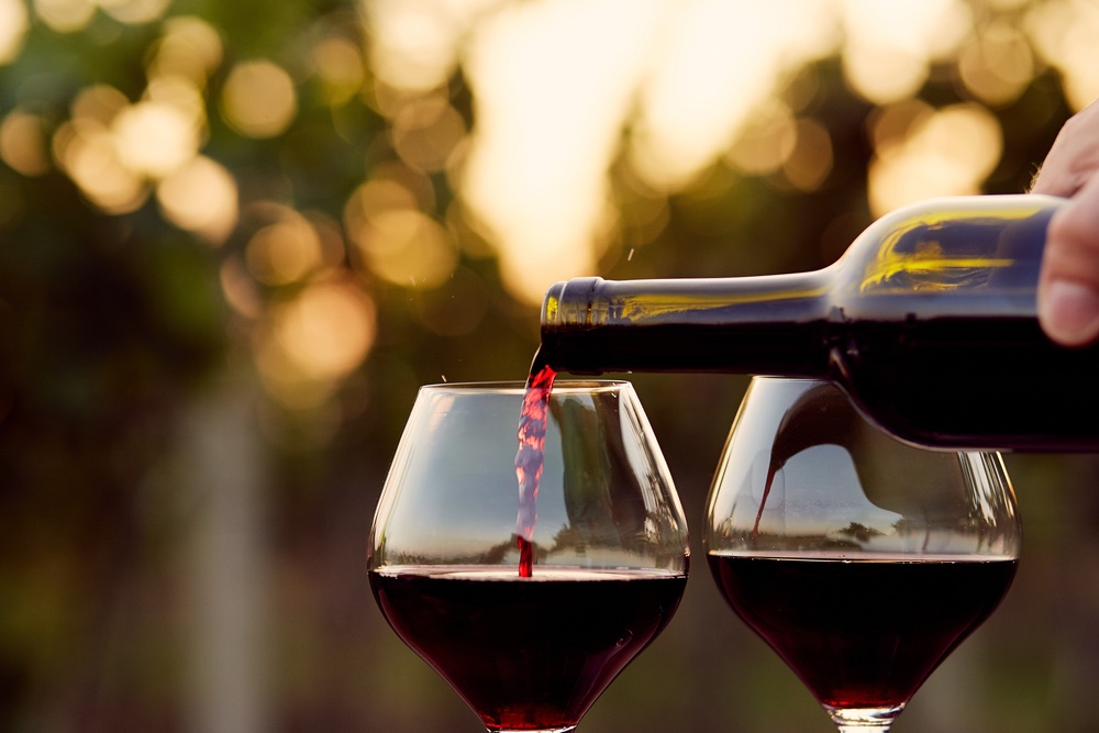Versare vino rosso da una bottiglia dentro due calici al tramonto