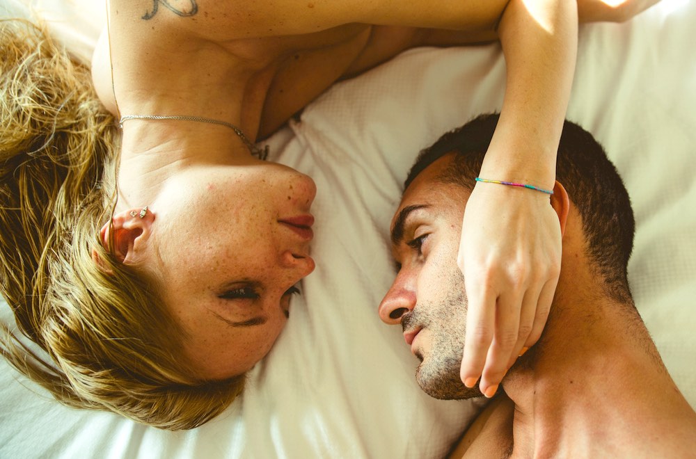 Una giovane coppia eterosessuale su letto con lenzuola bianche