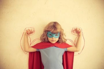 Bambina vestita da supereroe con maschera azzurra e mantello rosso