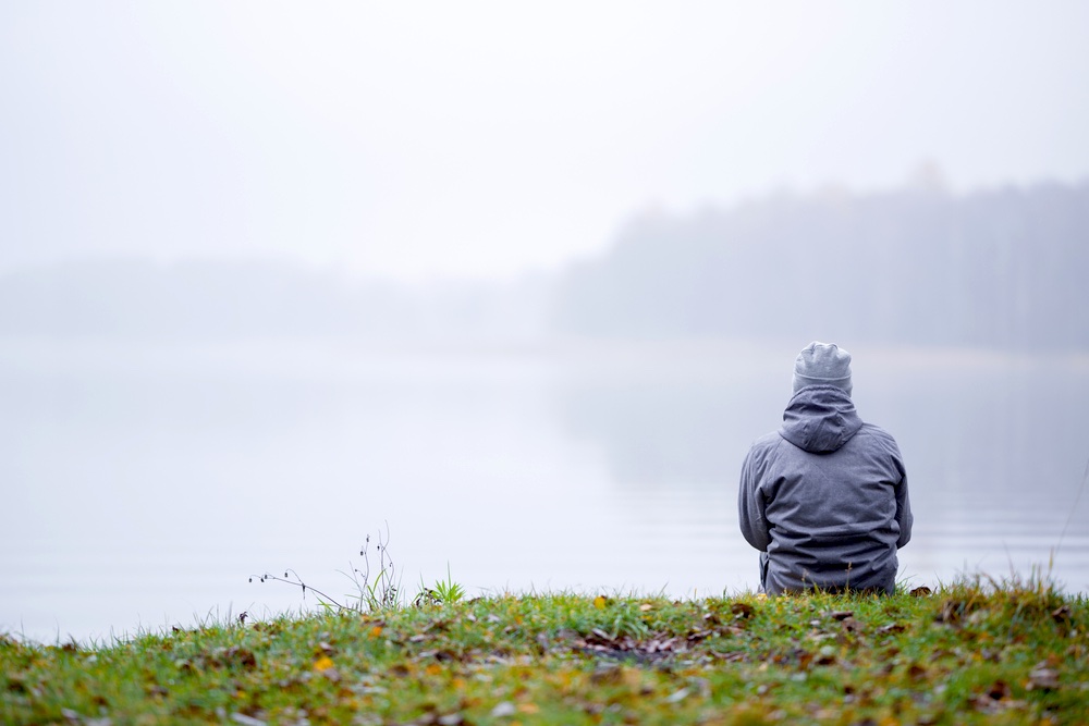 Ragazzo seduto sulle rive di un lago guarda la nebbia salire