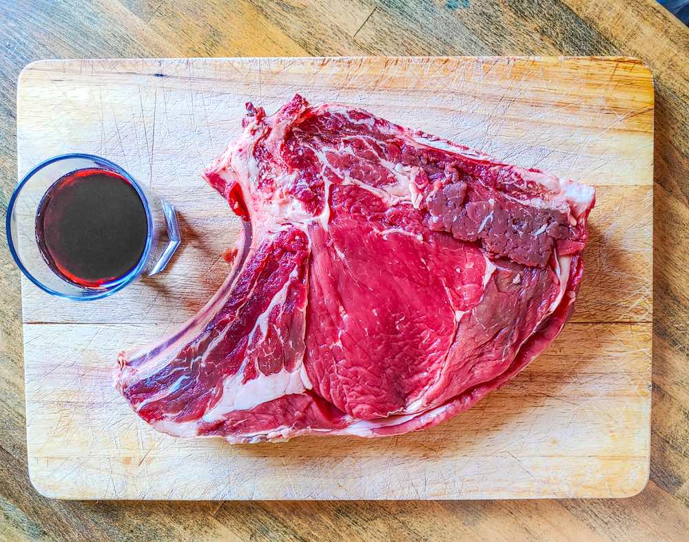 Una bistecca di carne chianina su un tagliere di legno con bicchiere di vino rosso