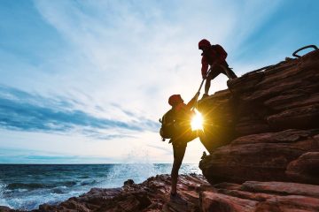 Una coppia di persone si aiutano a vicenda a scalare uno scogliera