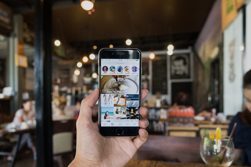 Uomo in un locale con un telefono in mano con schermata su Instagram