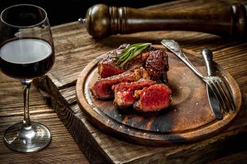 Calice di vino rosso con bistecca su tagliere di legno