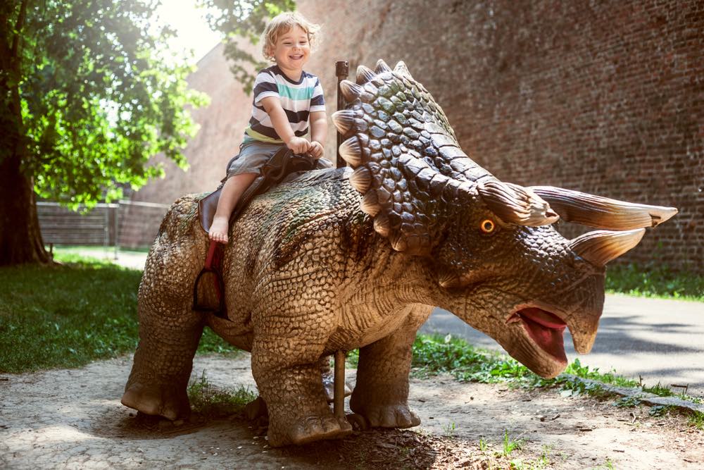 Bambino cavalca un dinosauro in un dino-park