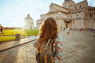 Turista elegante in abito floreale con zaino che fa un'escursione vicino alla cattedrale di Pisa.