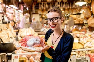 Giovane ragazza in un mercato con un piatto di salumi italiani in mano