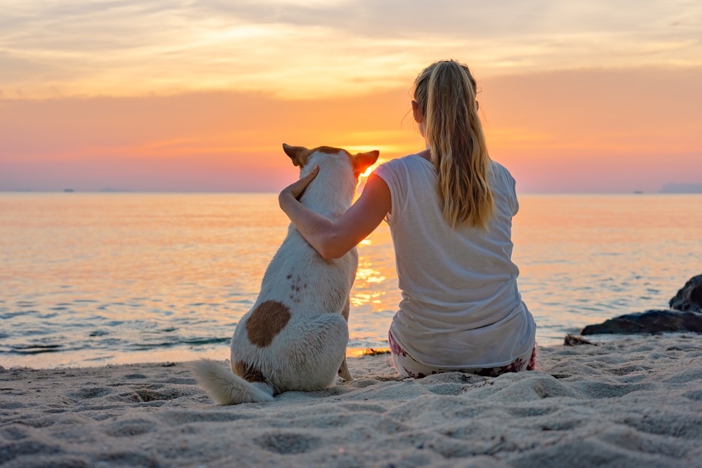 Donna con il proprio cane in spiaggia al tramonto