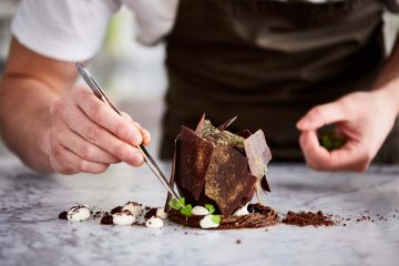 Fotografia di lifestyle di uno chef maschio dalla pelle chiara che prepara un dessert al cioccolato su una superficie di marmo