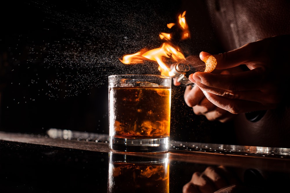 Bartender crea fiamme sopra un cocktail con arancia