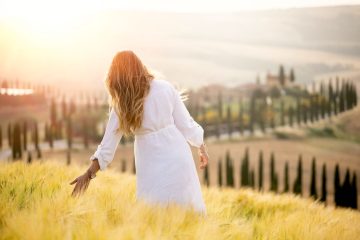 Ragazza vestita di bianco cammina per i campi di grano in Toscana