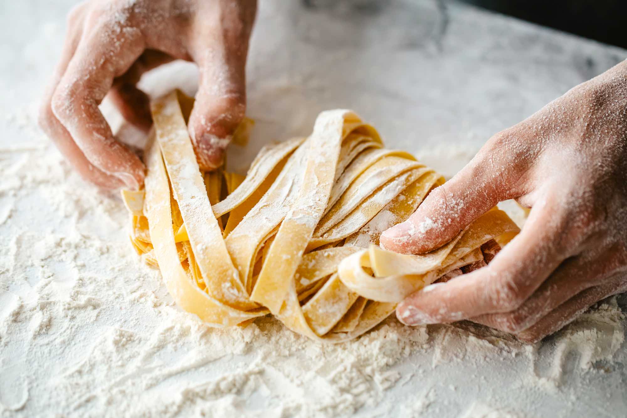 Farina sulle mani della chef che tira la pasta a un corso di cucina in Toscana