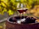 Bicchieri con vino rosso su botte con grappolo d'uva matura