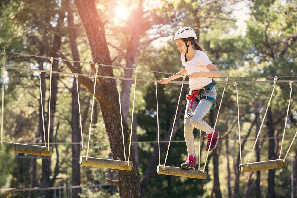 Bambina felice che si diverte in un parco avventura di arrampicata in una giornata estiva