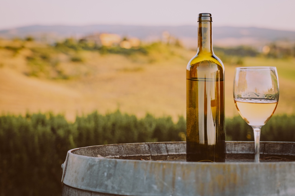 Bottiglia di vino su botte di vino davanti a vigne in Val d'Orcia