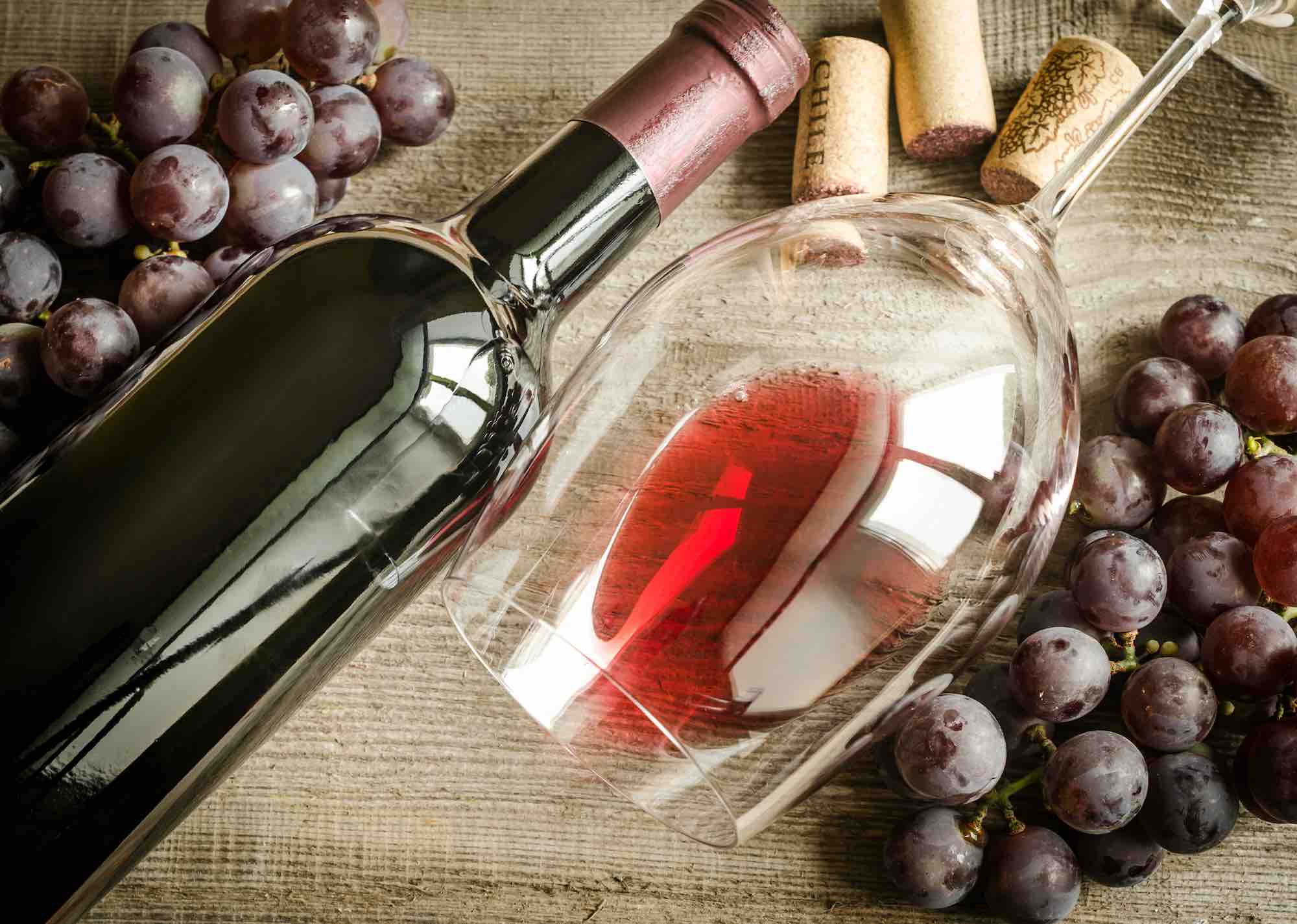 Bottiglia di vino rosso senza solfiti aggiunti con bicchiere e grappoli d'uva