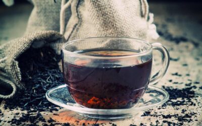 Tazza di vetro trasparente di tè nero e tè secco in bustine sullo sfondo di foglie di tè sparse sul vecchio sfondo di legno, messa a fuoco selettiva
