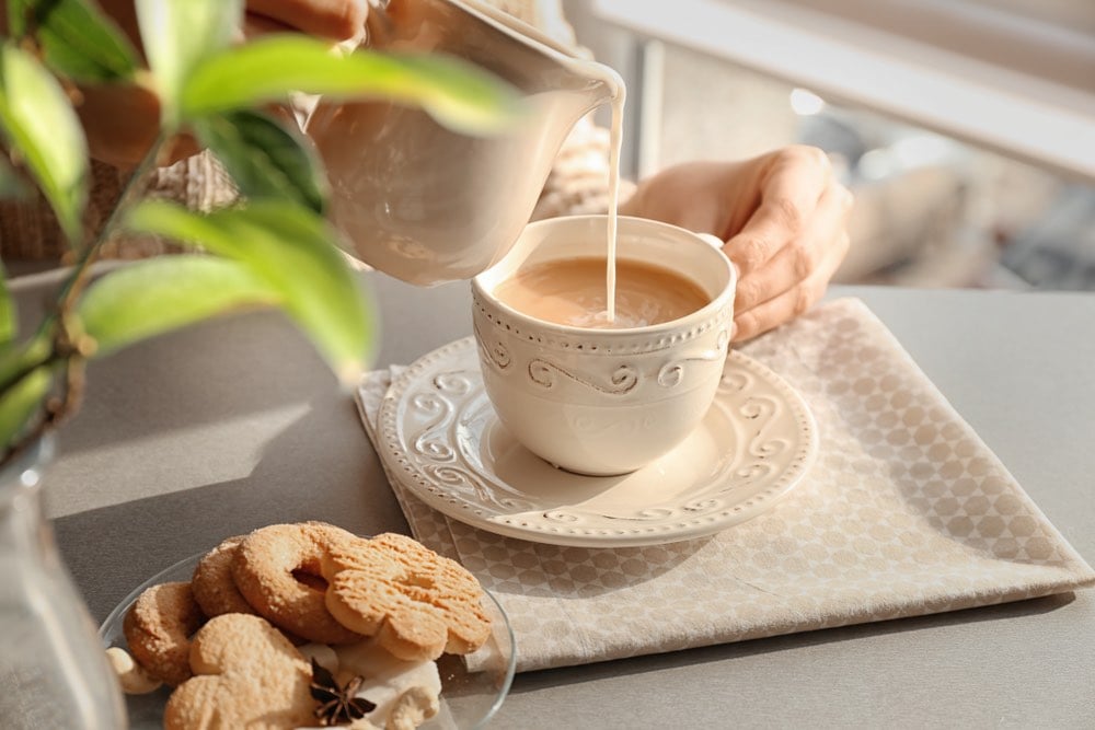 Donna che versa il latte in una tazza con tè aromatico sul tavolo