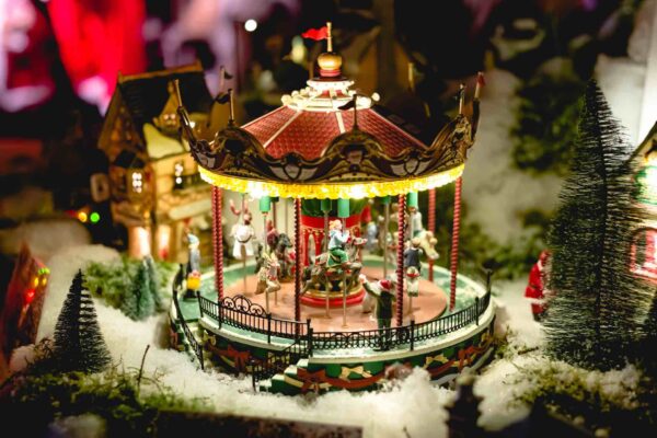 Giostra in miniatura della Fiera di Natale europea. Scena invernale della vigilia di Natale con case tradizionali in miniatura. Città notturna giocattolo vintage con carosello