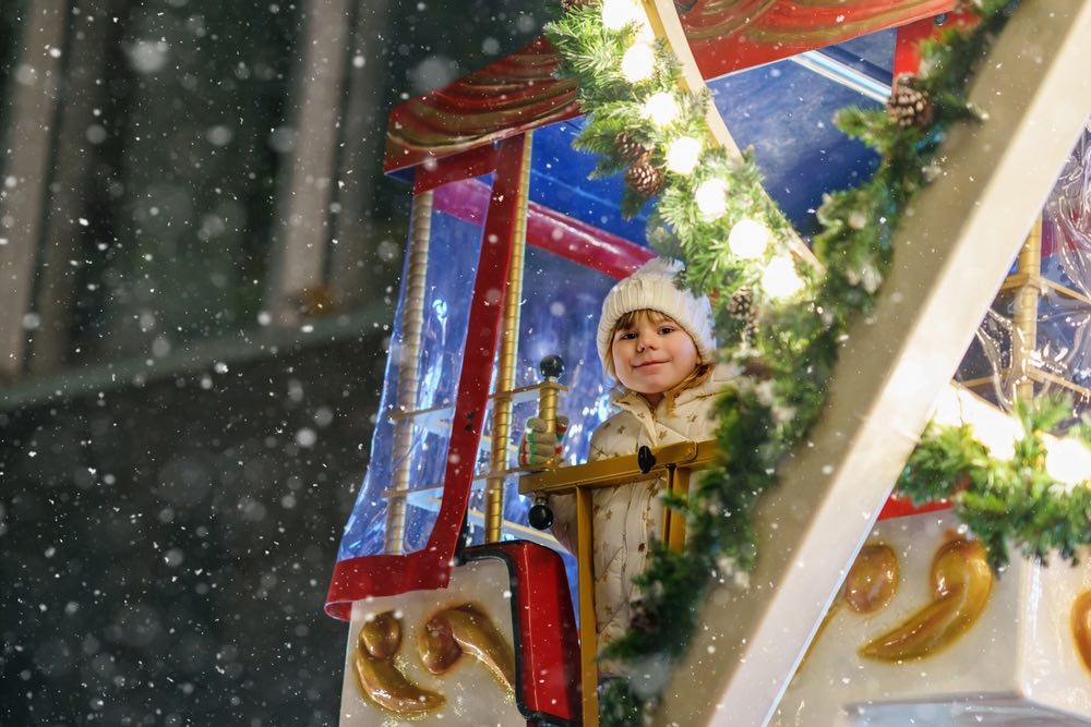 Piccola bambina in età prescolare sulla giostra della ruota panoramica al mercato di Natale