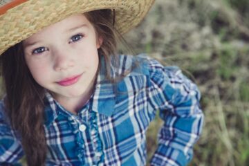 Bambina con camicia a quadri e cappello in una fattoria didattica