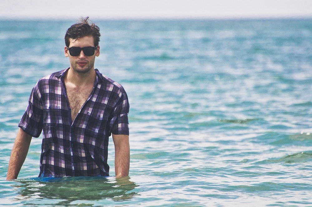 Ragazzo in camicia fa bagno in mare con occhiali da sole