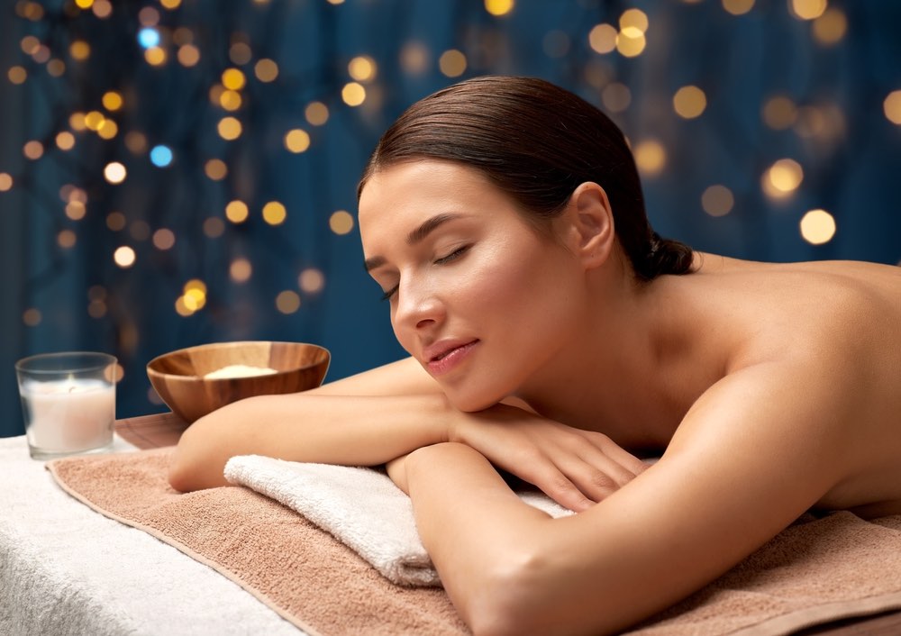 Concetto di benessere, bellezza e relax - giovane donna sdraiata in una spa o in un centro massaggi con luci dorate su sfondo blu