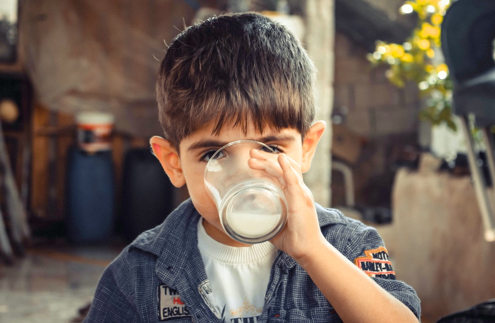 Bambino beve un bicchiere di latte