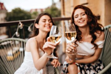 Due ragazze brindano con un calice di vino bianco in terrazza